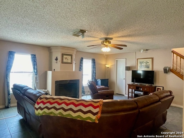 living area featuring a textured ceiling, a fireplace, visible vents, baseboards, and a ceiling fan