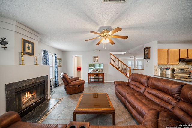 tiled living area featuring baseboards, a fireplace, stairway, a textured ceiling, and ceiling fan