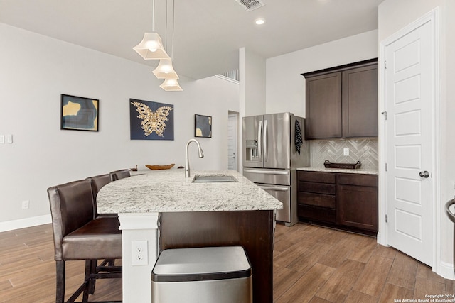 kitchen featuring hanging light fixtures, stainless steel fridge, a kitchen island with sink, hardwood / wood-style floors, and sink