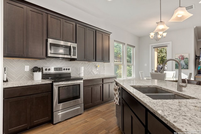 kitchen with pendant lighting, dark brown cabinets, light wood-type flooring, sink, and stainless steel appliances