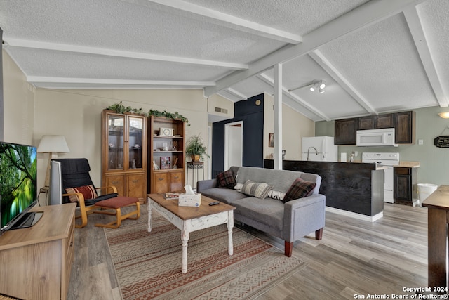 living room with a textured ceiling, vaulted ceiling with beams, sink, and light hardwood / wood-style flooring