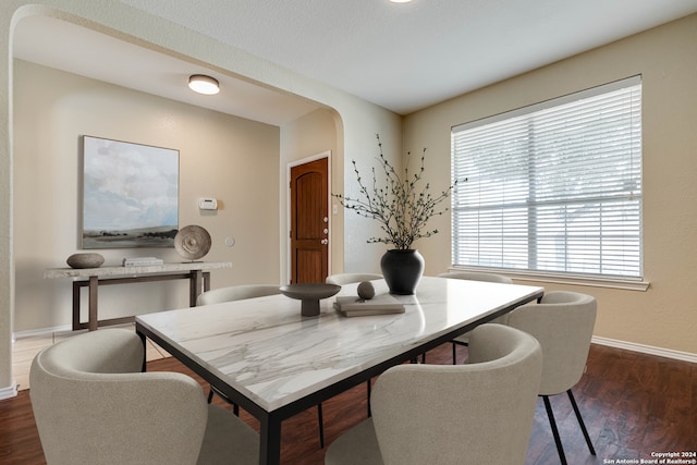 dining space featuring arched walkways, dark wood-type flooring, and baseboards