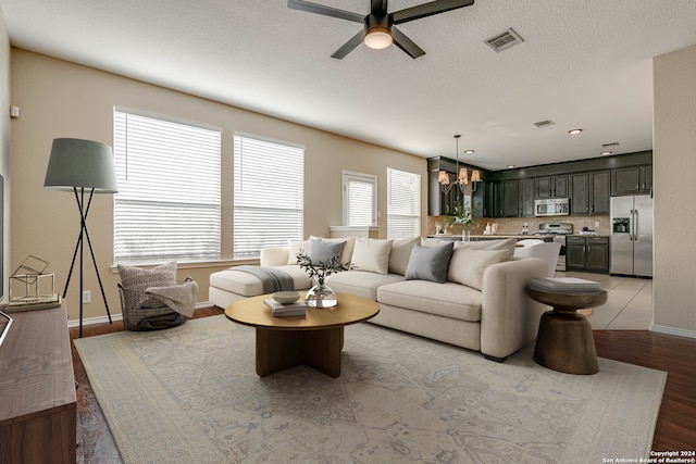 living area with a textured ceiling, ceiling fan with notable chandelier, visible vents, baseboards, and light wood-style floors