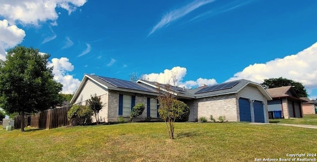 single story home featuring a front lawn, solar panels, and a garage