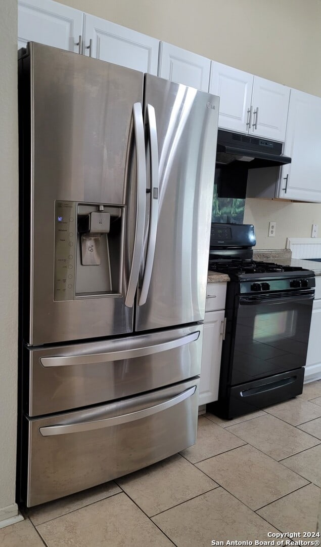 kitchen featuring black range with gas stovetop, stainless steel fridge, and white cabinetry