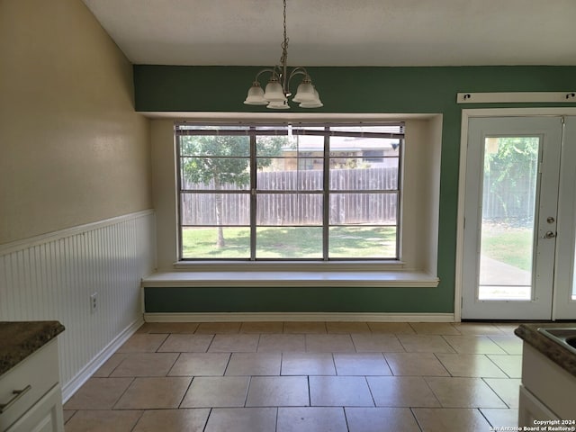 unfurnished dining area with light tile patterned floors, a chandelier, and a wealth of natural light