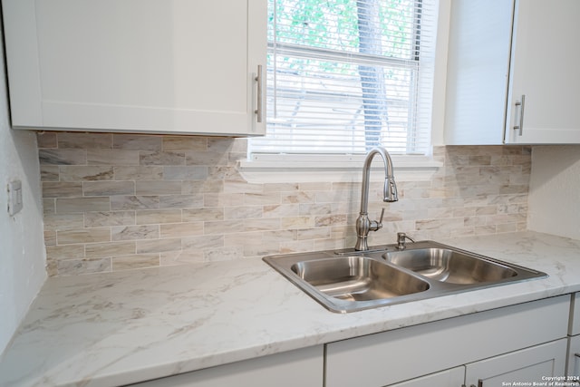 kitchen with decorative backsplash, white cabinetry, sink, and light stone counters