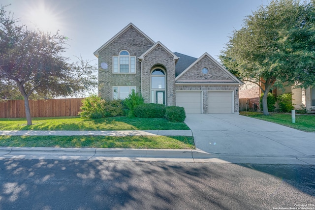 traditional-style home with a garage, brick siding, fence, driveway, and a front yard