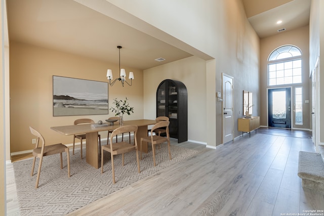 dining room with a chandelier, wood finished floors, a towering ceiling, visible vents, and baseboards