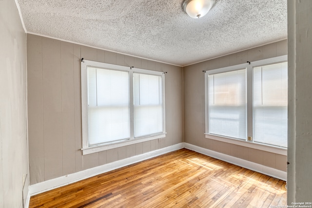 unfurnished room featuring a textured ceiling, light hardwood / wood-style floors, ornamental molding, and a wealth of natural light