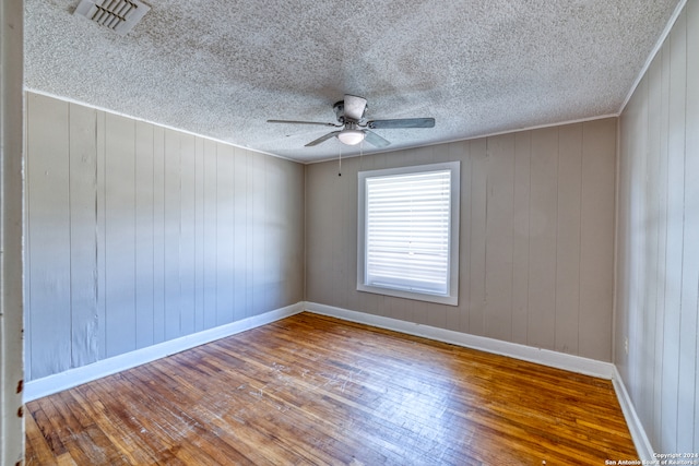 unfurnished room with ceiling fan, wood walls, and hardwood / wood-style floors