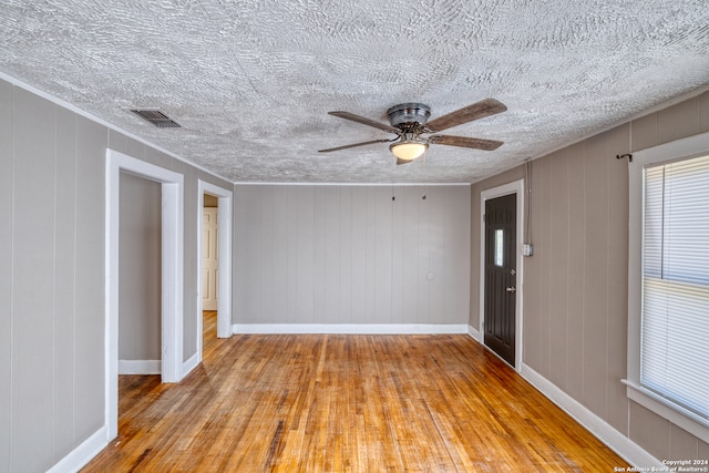 empty room featuring wood walls, light hardwood / wood-style floors, ceiling fan, and a textured ceiling