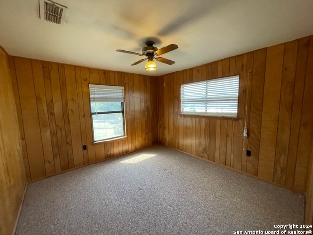 spare room featuring carpet, wood walls, and ceiling fan