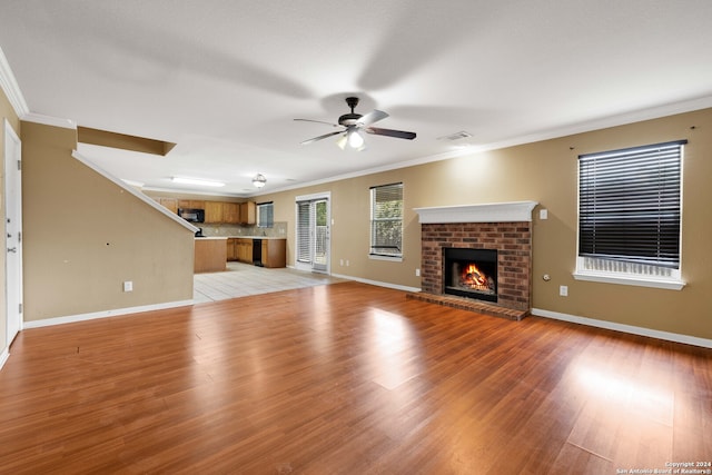 unfurnished living room with ceiling fan, a brick fireplace, light hardwood / wood-style floors, and crown molding