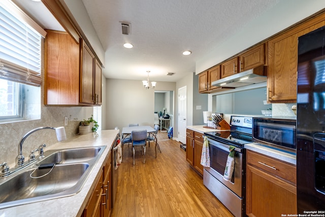 kitchen featuring tasteful backsplash, pendant lighting, black appliances, light hardwood / wood-style flooring, and sink