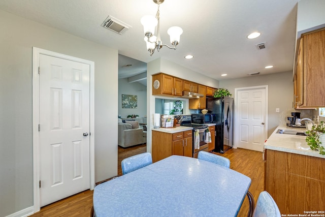 kitchen featuring brown cabinetry, light wood-style flooring, visible vents, black appliances, and a sink