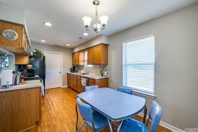 kitchen with baseboards, light wood-type flooring, a chandelier, brown cabinetry, and stainless steel dishwasher