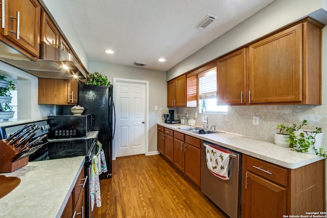 kitchen featuring sink, backsplash, extractor fan, black appliances, and light wood-type flooring