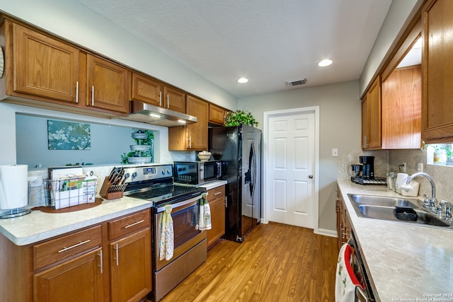 kitchen with light hardwood / wood-style flooring, sink, tasteful backsplash, and black appliances