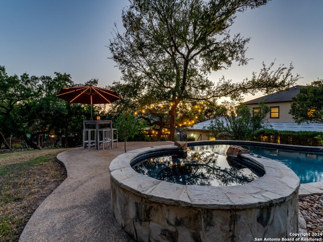 pool at dusk featuring a jacuzzi and a patio area