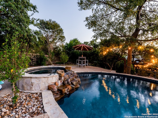 pool at dusk with an in ground hot tub