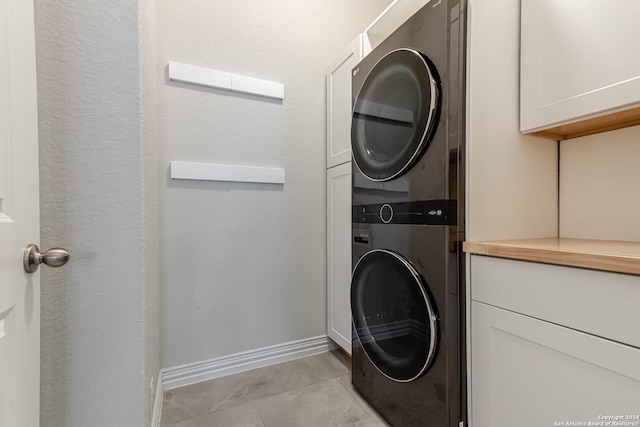 clothes washing area featuring cabinets and stacked washing maching and dryer