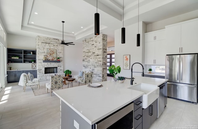 kitchen with white cabinets, a stone fireplace, pendant lighting, stainless steel appliances, and a kitchen island with sink