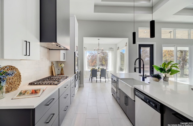 kitchen with pendant lighting, stainless steel appliances, wall chimney range hood, and sink