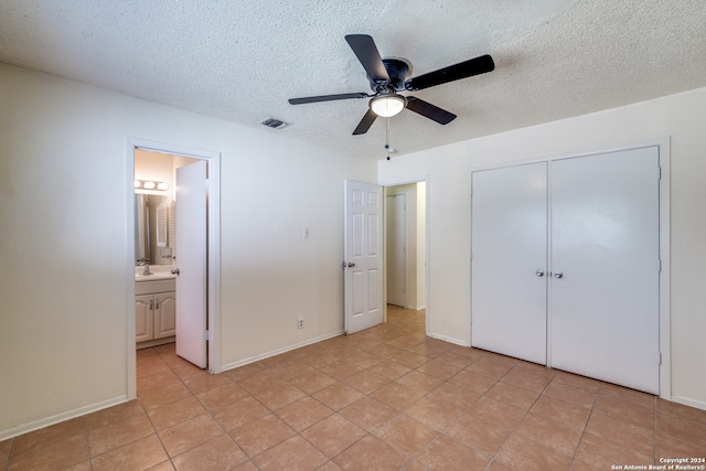 unfurnished bedroom with ceiling fan, light tile patterned floors, a textured ceiling, a closet, and ensuite bath