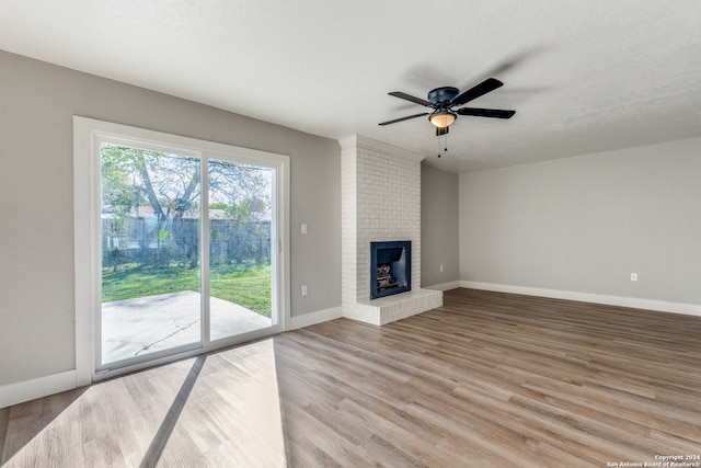 unfurnished living room featuring light wood-type flooring, ceiling fan, a fireplace, and a textured ceiling