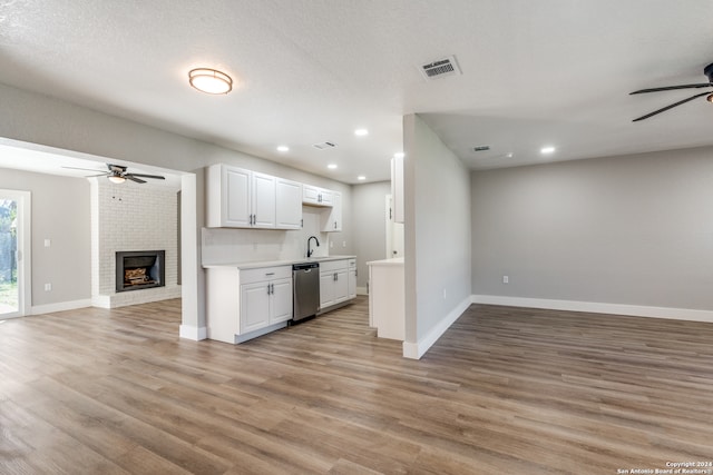 kitchen featuring dishwasher, ceiling fan, a brick fireplace, and white cabinets