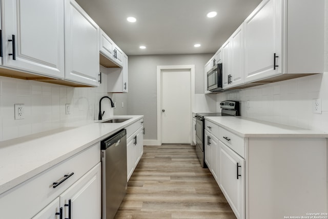 kitchen with sink, tasteful backsplash, white cabinetry, appliances with stainless steel finishes, and light hardwood / wood-style floors