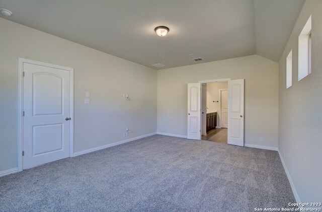 unfurnished bedroom featuring lofted ceiling, light carpet, and ensuite bath