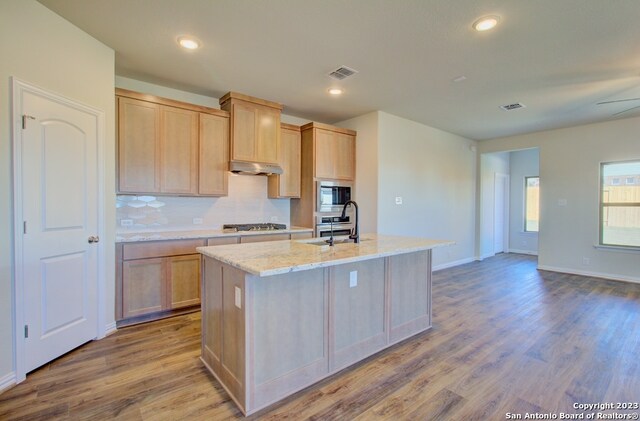 kitchen with light hardwood / wood-style floors, light brown cabinetry, built in microwave, and a kitchen island with sink