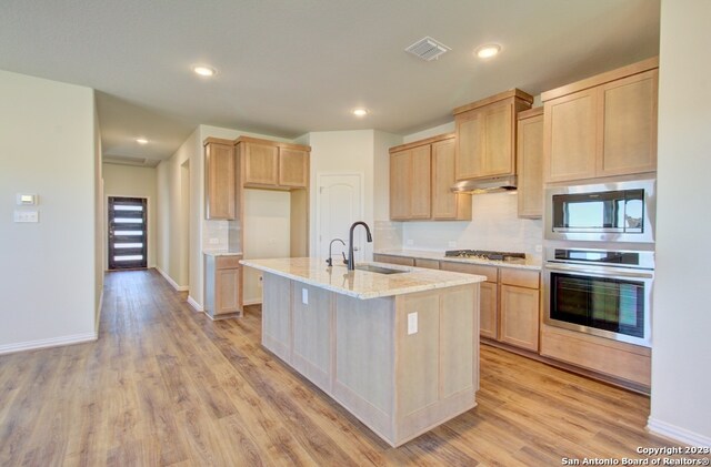 kitchen featuring light brown cabinetry, stainless steel appliances, a kitchen island with sink, sink, and light hardwood / wood-style flooring