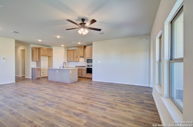 kitchen featuring light wood-type flooring, stainless steel oven, built in microwave, sink, and an island with sink