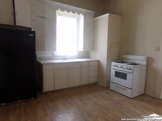 kitchen with black fridge, sink, white cabinets, light hardwood / wood-style flooring, and white range with gas stovetop