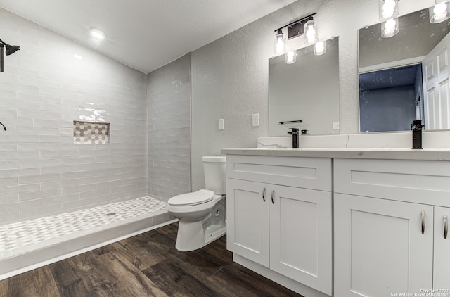 bathroom with vanity, toilet, tiled shower, hardwood / wood-style flooring, and vaulted ceiling