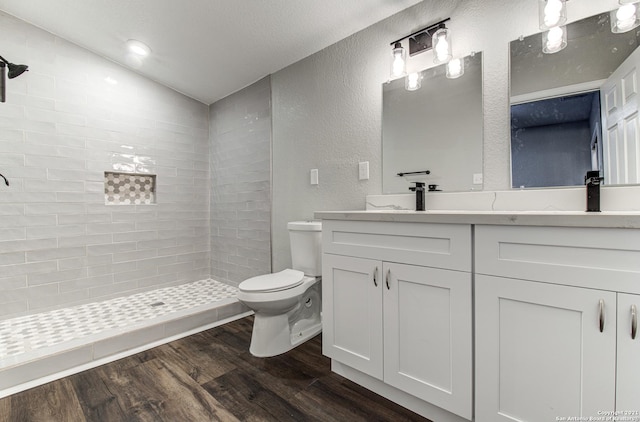 full bathroom with vaulted ceiling, a tile shower, toilet, a textured wall, and wood finished floors