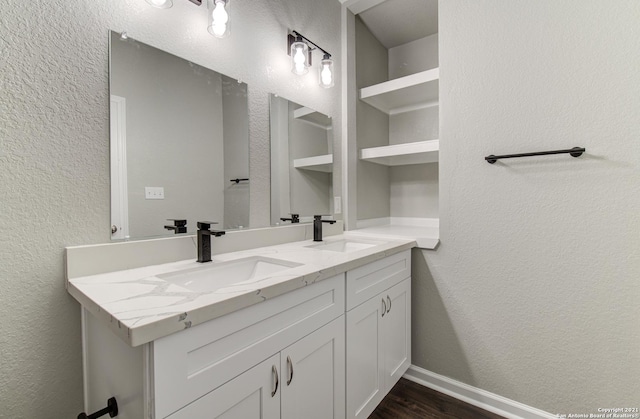 full bathroom with double vanity, a sink, baseboards, and wood finished floors