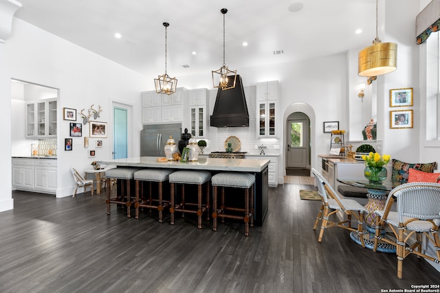 kitchen featuring dark hardwood / wood-style floors, white cabinetry, hanging light fixtures, custom range hood, and stainless steel built in fridge