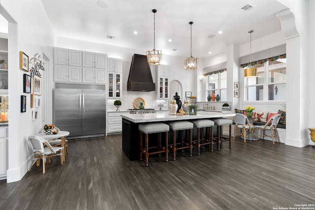 kitchen with decorative backsplash, a spacious island, premium range hood, dark hardwood / wood-style floors, and stainless steel built in fridge