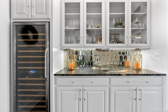 bar with dark stone countertops, white cabinets, beverage cooler, and decorative backsplash