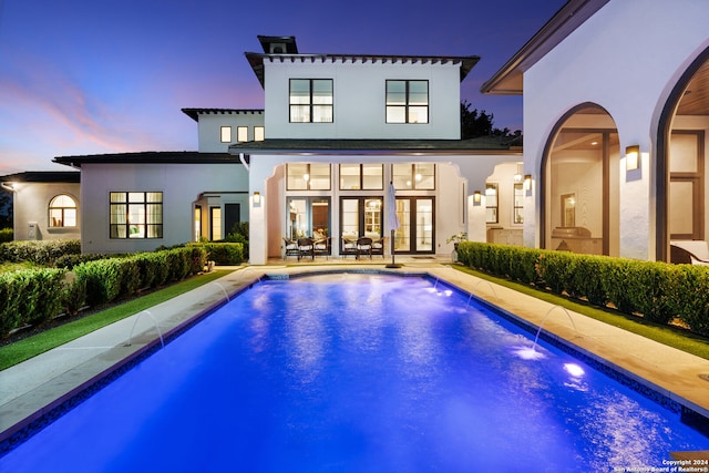 back house at dusk featuring pool water feature, a fenced in pool, a patio area, and french doors