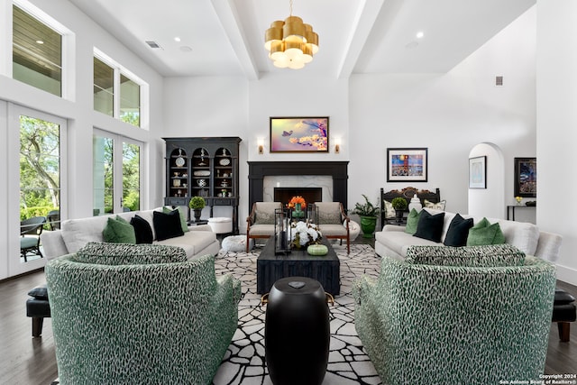 living room featuring wood-type flooring, a towering ceiling, an inviting chandelier, and a high end fireplace