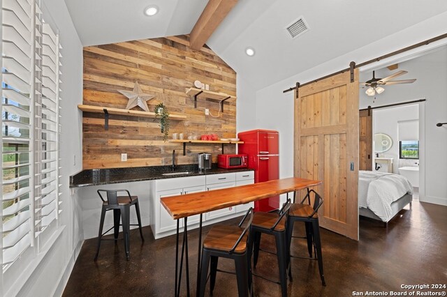 bar with a barn door, wood walls, ceiling fan, vaulted ceiling with beams, and white cabinetry