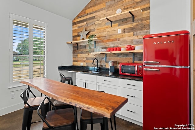 kitchen with lofted ceiling, stainless steel fridge, wooden walls, and white cabinetry