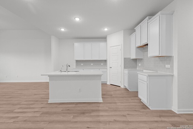 8432 Roadrunner Psge, San Antonio, TX 78222 - kitchen with light wood finished floors, a sink, decorative backsplash, a center island with sink, and baseboards