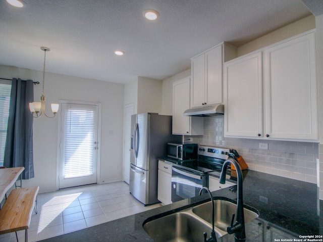 kitchen featuring white cabinets, light tile patterned flooring, appliances with stainless steel finishes, a notable chandelier, and dark stone counters