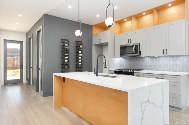 kitchen featuring appliances with stainless steel finishes, decorative light fixtures, an island with sink, decorative backsplash, and light stone counters